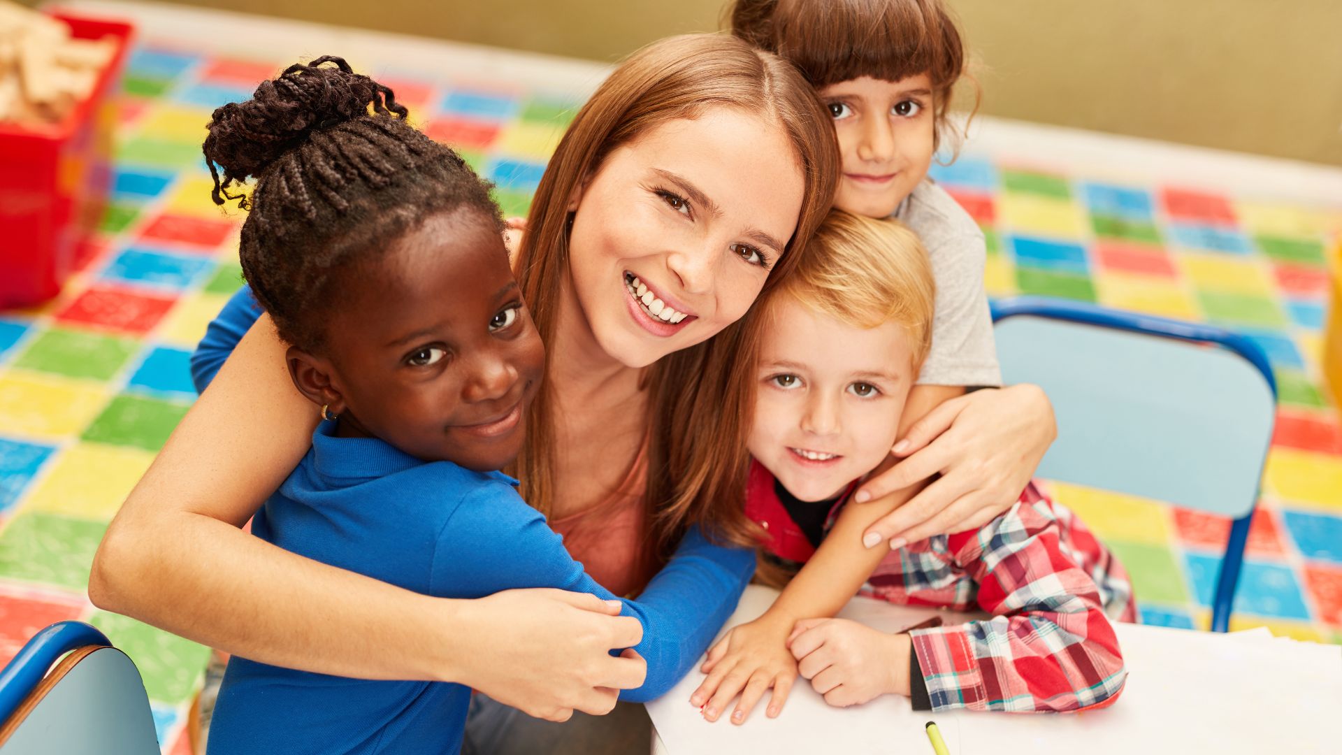 Teacher hugging three smiling children in classroom