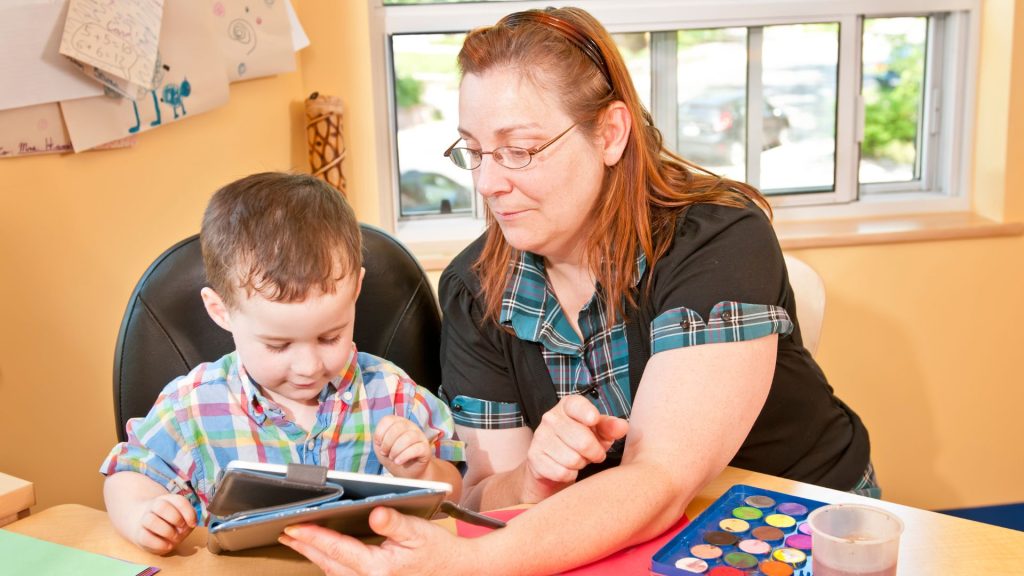 Teacher helping child with tablet in classroom