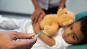 Child holding teddy bear, doctor with syringe.